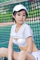 A woman in a white shirt and skirt sitting on a tennis court.