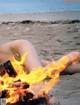 A woman laying on the beach next to a bonfire.