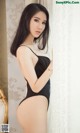 A woman in a black bodysuit leaning against a wall.