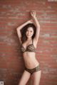 A woman in a leopard print bikini posing in front of a brick wall.