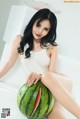 A woman sitting on top of a watermelon on a white surface.