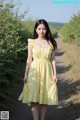 A woman in a yellow dress standing on a dirt road.