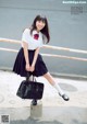 A woman in a school uniform holding a black bag.