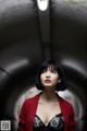 A woman in a black dress and red cardigan standing in a tunnel.