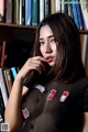 A woman in a black shirt sitting in front of a bookshelf.