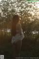 A woman standing in the middle of a forest at sunset.