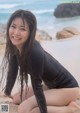 A woman in a wet suit sitting on the beach.