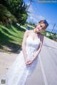 A woman in a white dress standing on the side of a road.